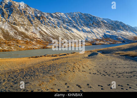 Die malerische Berg Herbst Landschaft mit Schnee bedeckte Berge, See, Sand Dünen mit spärlicher Vegetation gegen den blauen Himmel an einem sonnigen Stockfoto