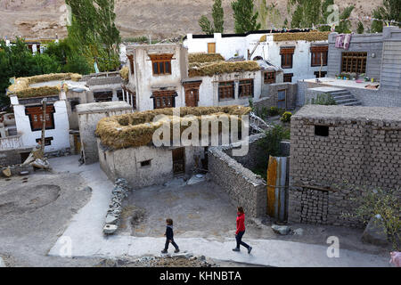 Kaukasische Mädchen und Jungen gehen in der schmalen Straße zwischen traditionellen Alchi Häuser, Ladakh, Jammu und Kaschmir, Indien. Stockfoto