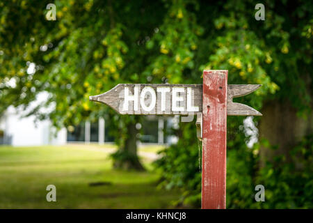 Hotel Schild in der Form eines Pfeils aus Holz, in einem Park mit einem Hotel im Hintergrund Stockfoto