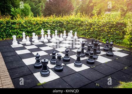 Großes Schach im freien Spiel auf einer Terrasse im Garten in einem Hof mit einer Hecke und Sonnenschein Stockfoto