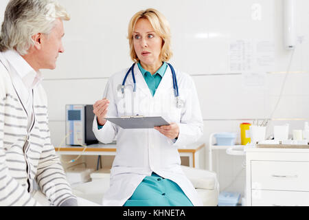 Hübsche Praktikerin, die einen ihrer Patienten während des Termins in der Klinik berät Stockfoto