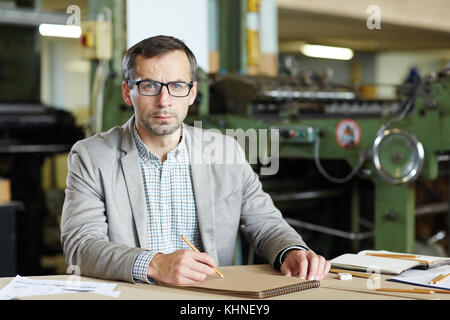 Ernst Ingenieur Skizzieren in Notepad von Arbeitsplatz auf dem Hintergrund von industriellen Maschinen Stockfoto