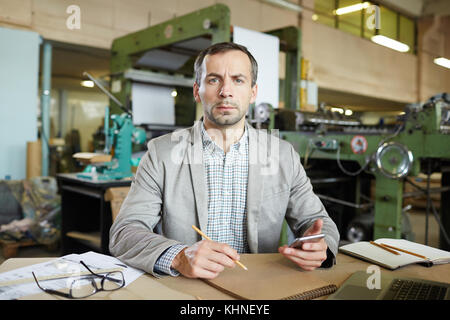 Zuversichtlich Meister mit Smartphone und Bleistift von Arbeitsplatz sitzen, Skizzieren und Kamera Stockfoto