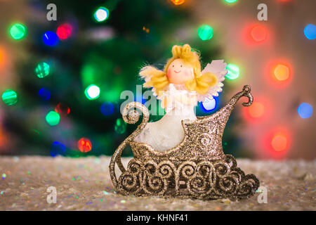 Weihnachten Spielzeug Engel in einem Schlitten vor dem Hintergrund der einen Weihnachtsbaum, Lichter von Girlanden, Bokeh Stockfoto