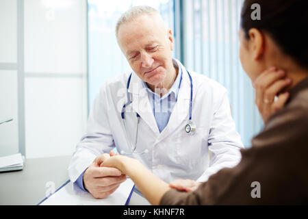 Reifer Kliniker, der junge Frau bei Hand hält und den Puls kontrolliert Stockfoto