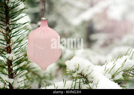 Vintage Glas matt Rosa Weihnachtsbaum Verzierung unter den schneebedeckten Zweigen vor dem Hintergrund einer verschwommenen echten Winter Forest Stockfoto