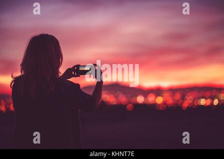 Malerische vista Bilder nehmen Sie ihr Smartphone integrierten digitalen Kamera. Frau, die während der malerischen Sonnenuntergang. die Skyline der Stadt. Stockfoto