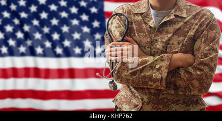 Soldat mit Stethoskop in amerikanischer Uniform, stehend auf einer USA-Flagge im Hintergrund Stockfoto