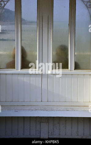 Zwei Menschen, ein Mann und eine Frau sitzen auf einem Sitz in einem viktorianischen Zuflucht auf Cromer Pier in Norfolk. steamy Glas mit Meer und Küste in der Ferne. Stockfoto