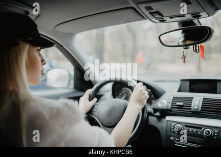 Frau in dem Auto innen hält Rad drehen um lächelnd mit Blick auf die Fahrgäste im Fond Idee Taxifahrer. Konzept der Untersuchung Fahrzeug. Stockfoto