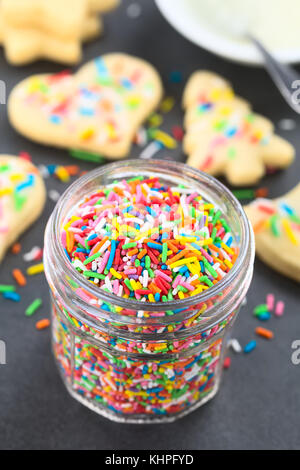 Bunter Zucker Streusel in Glas Glas mit Dekor Sugar Cookies und Puderzucker in einer Schüssel in der Rückseite, fotografiert auf Schiefer (selektive Fokus) Stockfoto