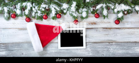 Weihnachten Hintergrund mit Santa Claus hat und elektronischen Notizbuch mit traditionellen Dekorationen auf rustikalen weissem Holz. Stockfoto