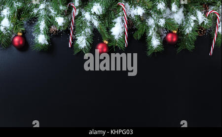 Snowy christmas tree branches, Zuckerstangen und roten Ornamenten auf schwarzem Hintergrund Stockfoto