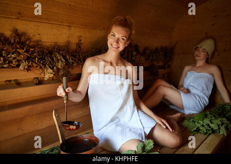 Zwei schöne junge Frauen in Handtüchern relaxen in Holz- Sauna. in Schuß mit natürlichem Licht. Stockfoto