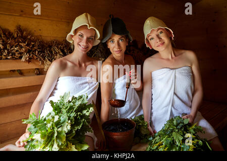 Drei schöne junge Frauen in Handtüchern relaxen in Holz- Sauna. in Schuß mit natürlichem Licht. Stockfoto