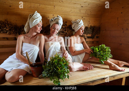 Drei schöne junge Frauen in Handtüchern relaxen in Holz- Sauna. in Schuß mit natürlichem Licht. Stockfoto