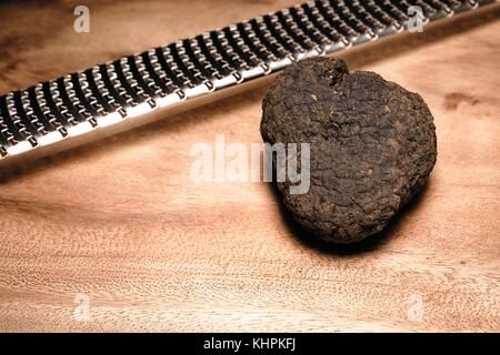 Seltene schwarze italienische Trüffel und metallreibebrett auf einer hölzernen Schneidebrett Stockfoto