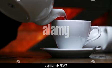 Frau gießen Tee aus Weißer Wasserkocher zu Tasse im Cafe Stockfoto