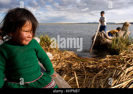 Insel Uros, Titicacasee, peru, Südamerika. Kinder segeln in einem Totora-Boot auf dem Titicacasee in der Nähe einer Insel, die von Uros bewohnt wird. Stockfoto