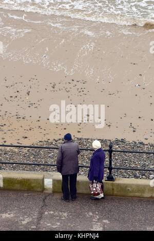 Und ältere Paare tragen Mäntel und Hüte zu Fuß entlang der Strandpromenade in cromer in Norfolk an einem Wintertag. Ruhestand zu Fuß entlang der Strandpromenade am Strand Stockfoto