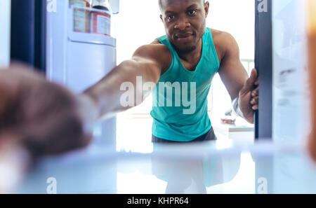 Ein Mann, der zu Hause etwas in den Kühlschrank stellt. Fitnessbegeisterte nutzen nach dem Training einen Kühlschrank. Stockfoto