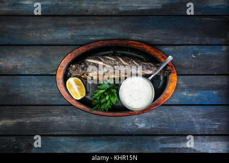 Pfanne mit leckeren Forellen fischen auf hölzernen Hintergrund Wein Grüns, Sauce und Zitrone. Stockfoto