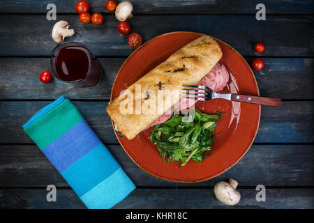 Sandwich mit Schinken, Pilzen und grünem Salat auf einer Keramikplatte. farbige Holz- Hintergrund. Ansicht von oben. Stockfoto