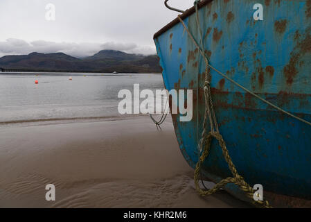 Vor einem rostigen alten blauen Fischerboot an einem Sandstrand in tywyn Mündung, abermaw, Wales mit Liegeplatz Seile befestigt Stockfoto