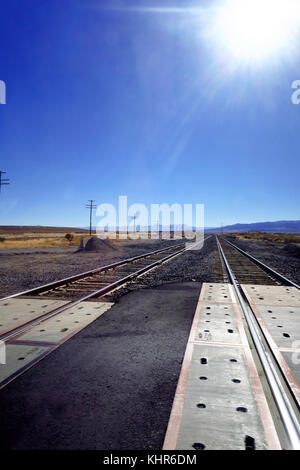 Zwei Eisenbahnschienen an einer Kreuzung Leuchten durch Solar Flare auf einem strahlend blauen Himmel. Stockfoto