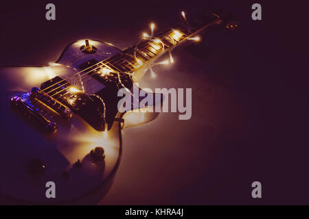 E-Gitarre mit beleuchtete Girlande auf dunklem Hintergrund. Geschenk Gitarre klassische Formen für Weihnachten oder Neujahr. Stockfoto