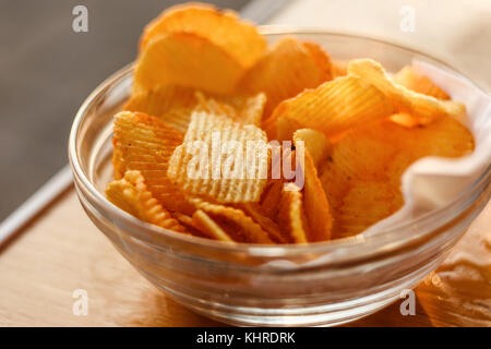 Kartoffelchips in Schüssel auf hölzernen Tisch bei Sonnenuntergang Stockfoto