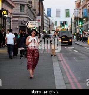 Asiatische Frau mit ihrem Smartphone während Wandern auf der Oxford Street, London, England Stockfoto
