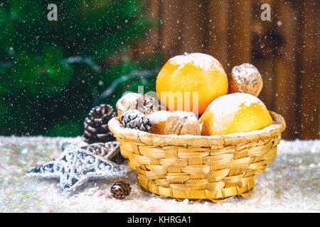 Mandarinen, Nüsse und Stösse in einem Korb auf dem Hintergrund einer Weihnachtsbaum Stockfoto