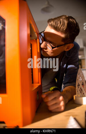 Portraitfotos von neugierigen jungen Ingenieur lehnte sich auf Büro Schreibtisch und achten Sie dabei auf Verfahren des 3D-Drucks Stockfoto