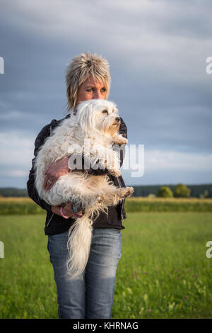 Hält eine Frau ihre kleine weißn Hund in ihre Arme. Stockfoto