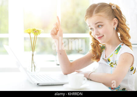 Hübsches kleines Mädchen mit modernen Laptop am Tisch sitzen Stockfoto