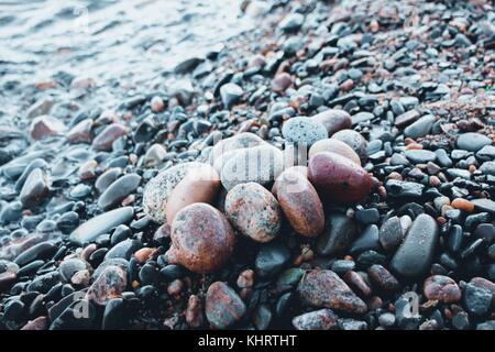Steine in verschiedenen Farben und verschiedenen ovale Formen liegen auf dem steinigen Ufer eines großen und kalten See. Stockfoto