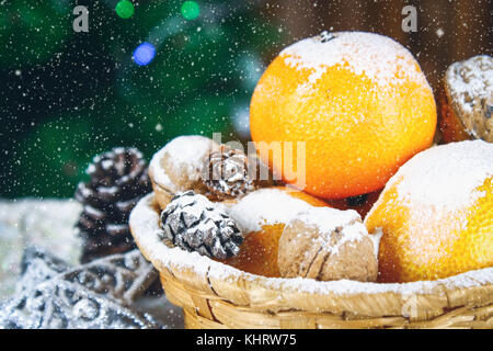 Mandarinen, Nüsse und Stösse in einem Korb auf dem Hintergrund einer Weihnachtsbaum Stockfoto