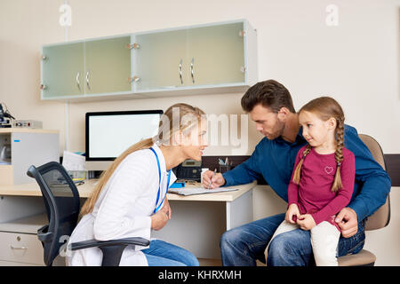 Portrait des jungen Mannes Unterzeichnung Patienten Form sitzen im Doktorbüro beim Besuchen der Kinderarzt mit seiner kleinen Tochter Stockfoto