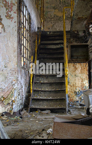 Treppen mit gelben Geländer in einem zerstörten industriellen Interieur. verlassene alte Fabrik. Stockfoto