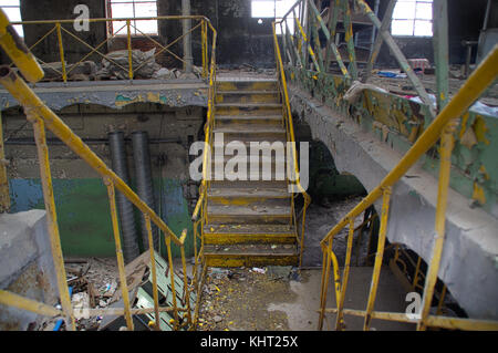 Treppe mit gelben Geländer in einem zerstörten industriellen Interieur. Vergessen alte Fabrik. Stockfoto