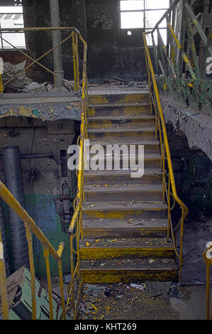 Treppe mit gelben Geländer in einem zerstörten industriellen Interieur. Vergessen alte Fabrik. Stockfoto