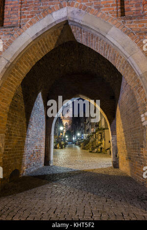 Alte Gebäude auf dem st.Mary Street und St. Mary's Kirche in der Stadt (Altstadt) in Danzig, Polen, durch eine gewölbte Tor bei Nacht gesehen. Stockfoto