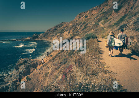 Junges Paar zu Fuß auf einem robusten Trail mit ihren Surfboards in Palos Verdes Estates, Kalifornien Stockfoto