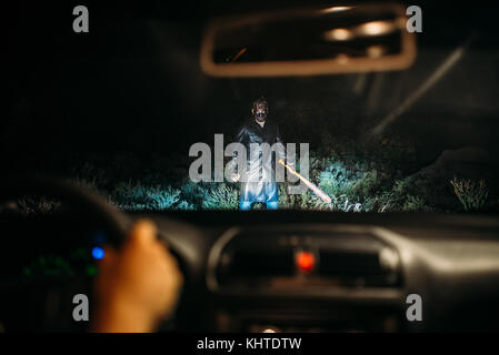 Serial maniac im Hockey Maske mit blutigen Baseballschläger in der Kette in der Weise steht der weiblichen Opfer auf das Auto in der Nacht gehüllt. Horror, Mörder Stockfoto