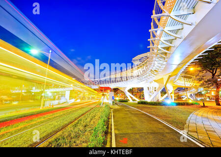 Blick auf eine moderne Straßenbahn-Station mit einer Straßenbahn auf der Durchreise in der Nacht in Kaohsiung, Taiwan. Stockfoto