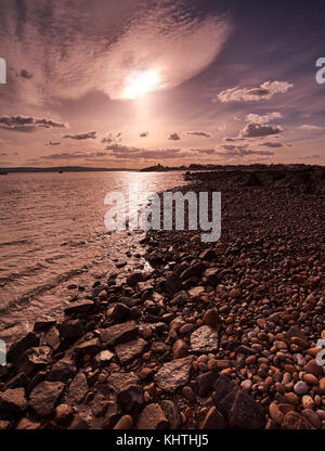 Blick vom Kiesstrand an Lindisfarne (Heilige Insel) auf dem Festland bei Sonnenuntergang, Großbritannien Stockfoto