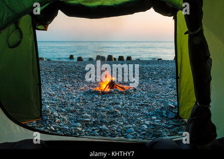 Blick auf das Lagerfeuer am Strand vor dem Hintergrund des Meeres von Zelt der Tourist Camp bei Sonnenuntergang gesehen Stockfoto