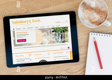 Der Sainsbury Bank Website auf einem iPad Tablet Gerät, das auf einem Tisch liegt neben einem Notizblock und Bleistift und eine Tasse Kaffee (nur redaktionell) Stockfoto