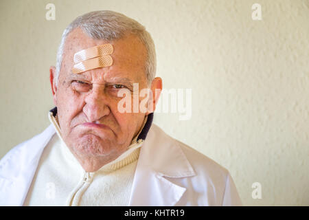 Alte Doktor mit Flecken auf der Stirn schmollend Stockfoto